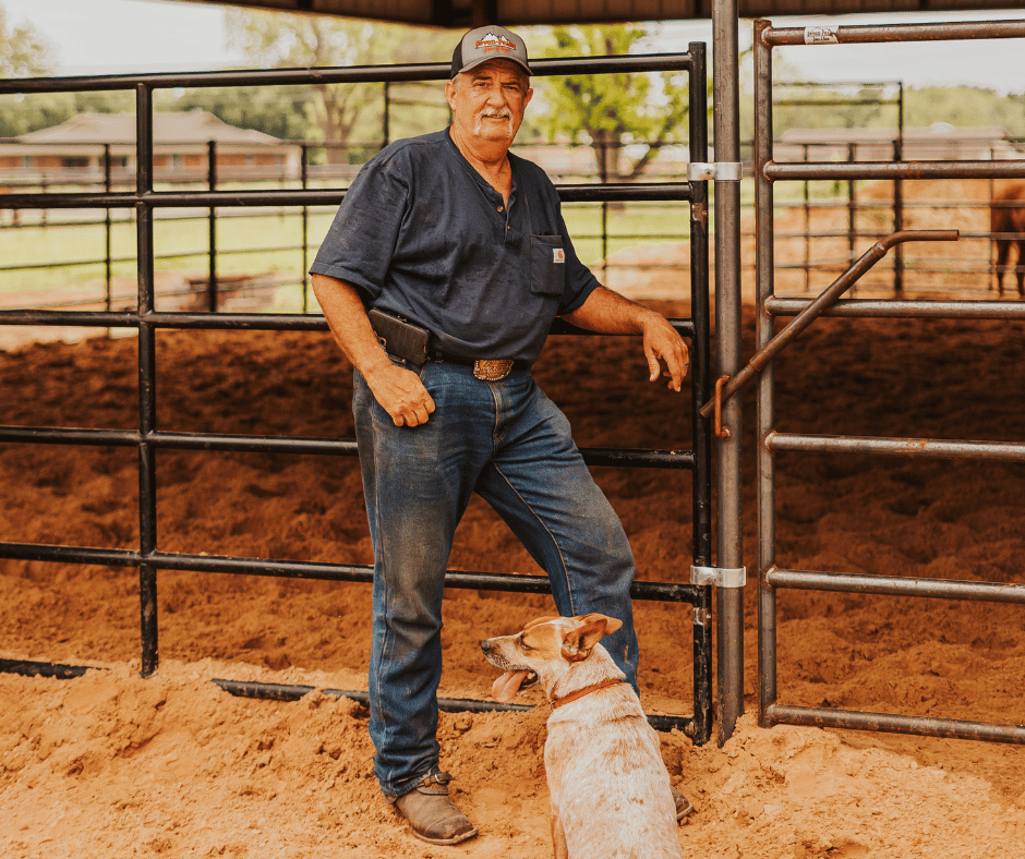 Man in ranch with dog standing by fence.