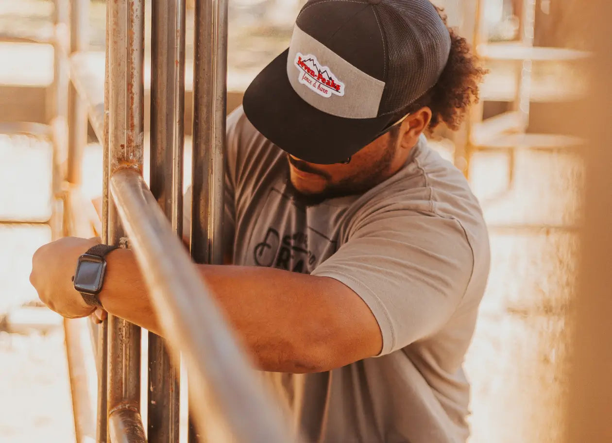 A man in a Seven Peaks Hat and grey Tshirt installing a metal fence